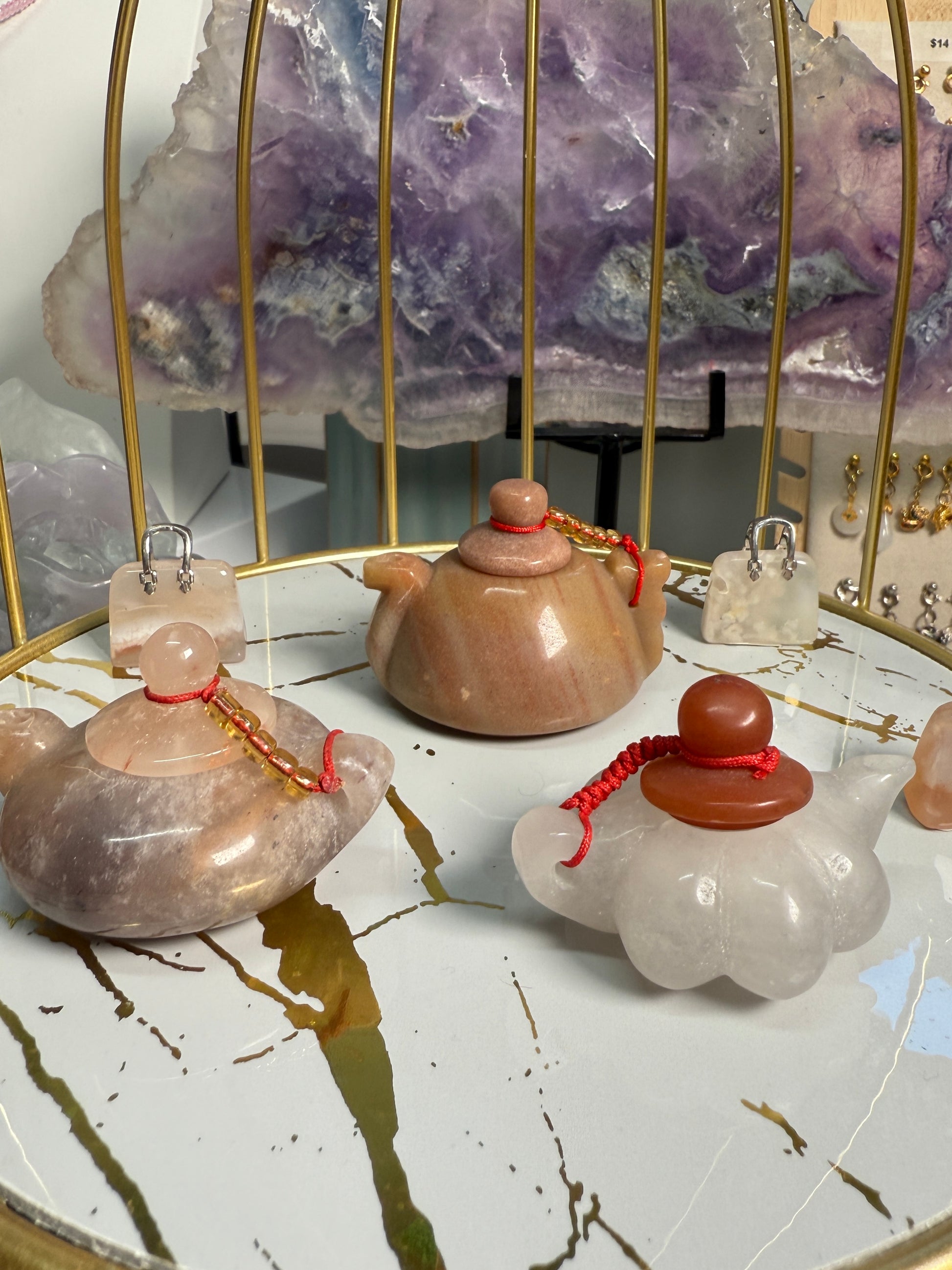 Image of three mini crystal teapots displayed —White Jade, Golden Jasper, and Purple Jade—each polished and carved in a classic teapot shape. The 2-inch figurines are arranged on a flat surface as elegant decorative accents.